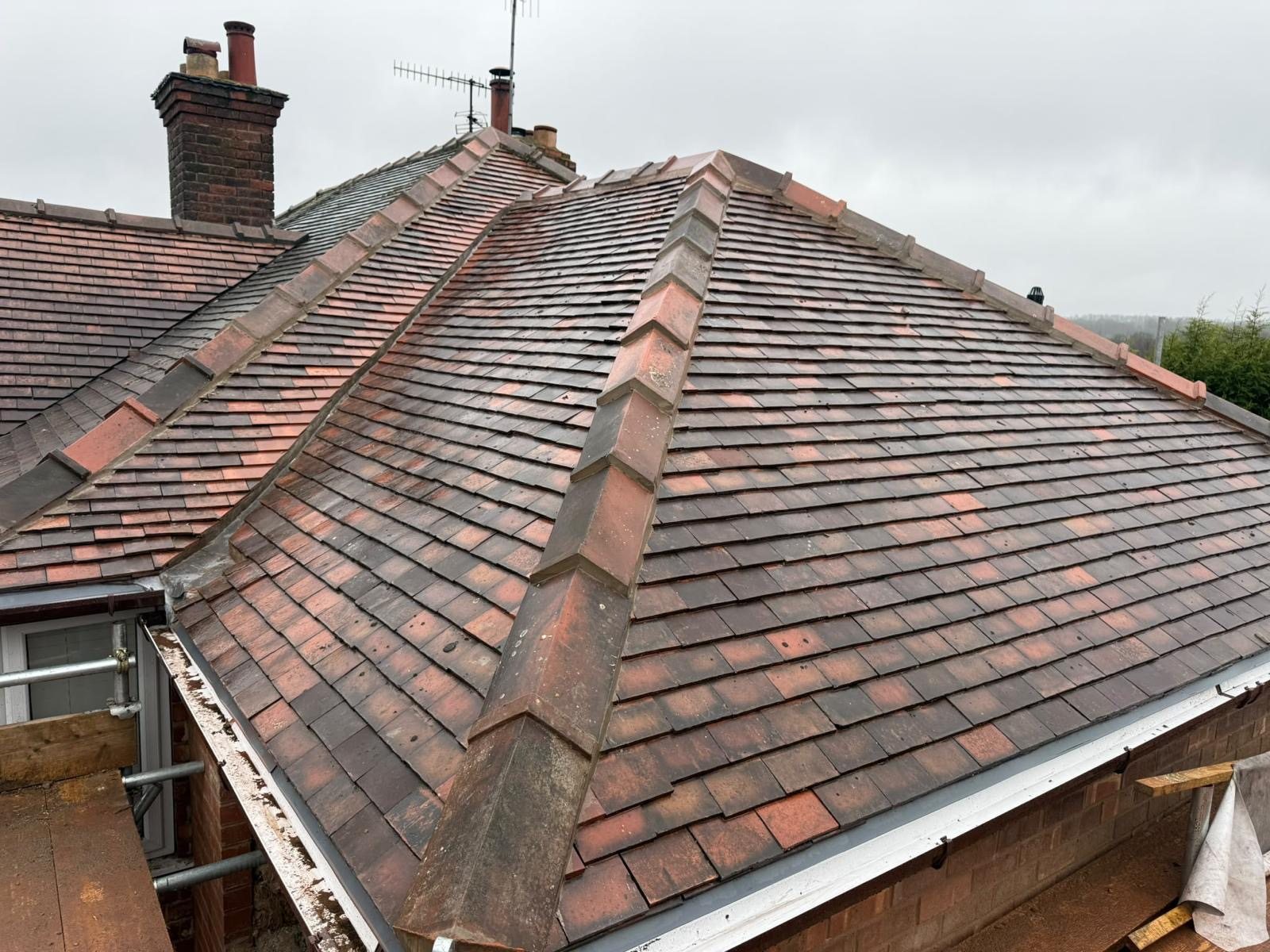 New hipped roof in red-brown clay plain tiles with bonnet hip tiles and a new white fascia, under an overcast sky