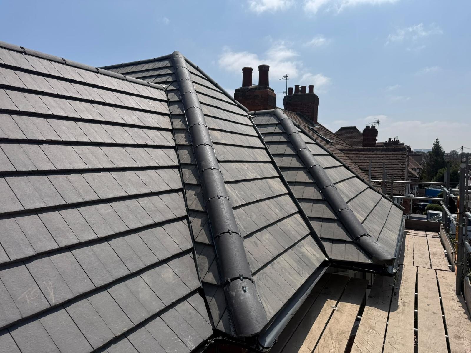 New grey slate-effect tiled hipped roof with dry-fix hip ridges, scaffold in the foreground